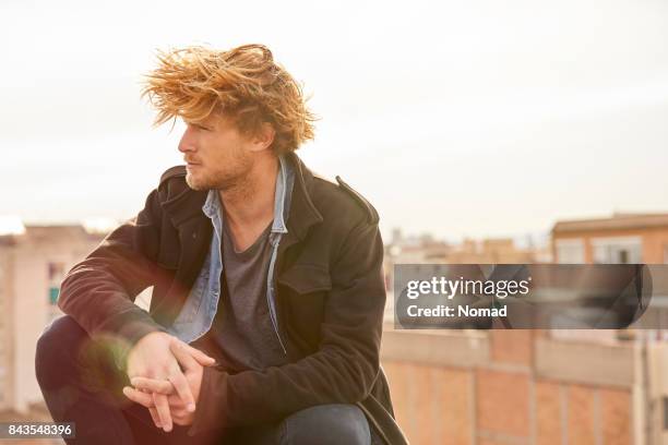 thoughtful handsome man sitting at rooftop - tousled hair stock pictures, royalty-free photos & images