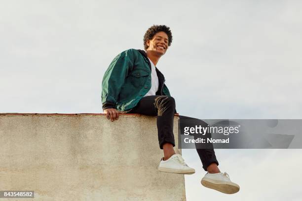 portrait of smiling carefree man at rooftop - sitting stock pictures, royalty-free photos & images