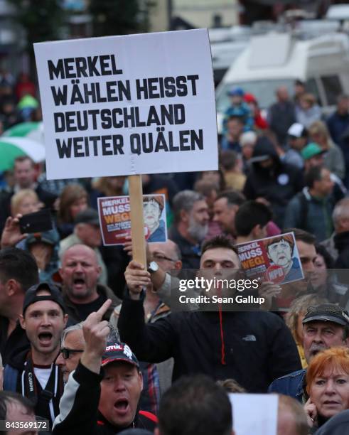 Protesters and hecklers, among them supporters of the far-right NPD political party, hold up pieces of paper that read: "Merkel muss weg!" as another...