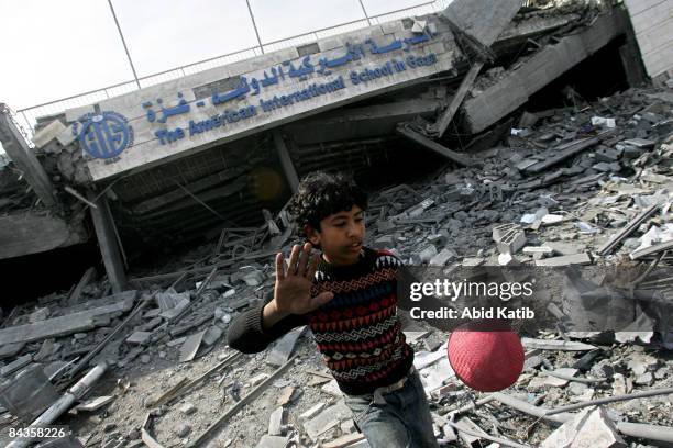 Palestinian boy holds a ball as he walks on the rubble of the American International School, which was destroyed by an Israeli air strike January 19,...