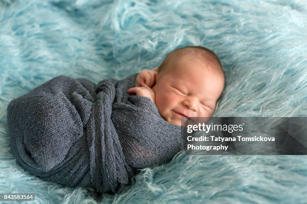 happy smiling newborn baby in wrap, sleeping happily in cozy blue fur, cute infant baby - babydecke stock-fotos und bilder