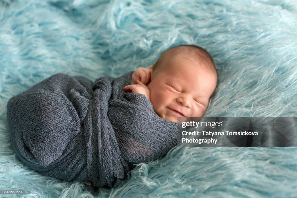 Happy smiling newborn baby in wrap, sleeping happily in cozy blue fur, cute infant baby