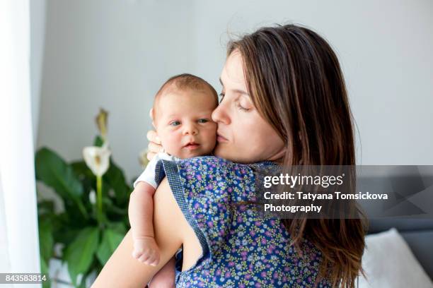 young mother, kissing and hugging her newborn baby boy, tender, care, love, positive emotions - new mother stock pictures, royalty-free photos & images