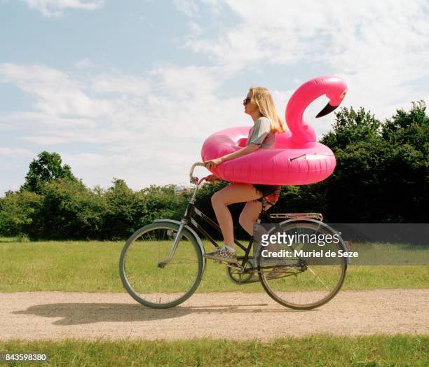 young woman cycling with flamingo ring - fun stockfoto's en -beelden