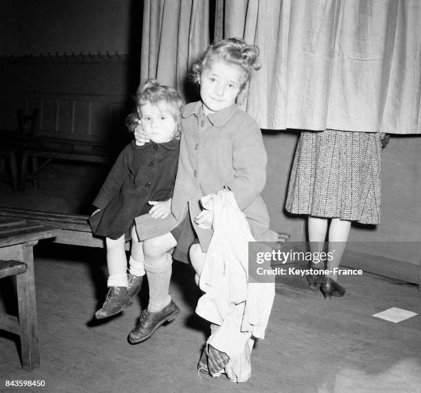 Dans un bureau de vote, un bébé et son petit frère attendent devant l'isoloir où se trouve leur maman qui vote, à Paris, France en 1946.