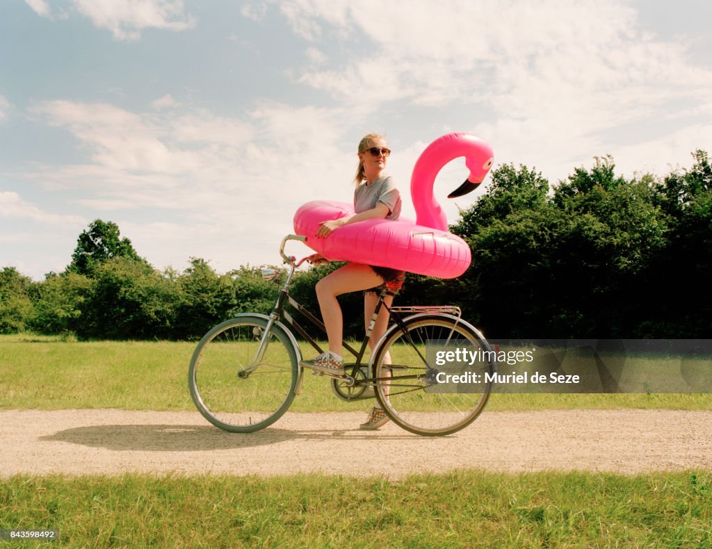 Young woman on bicycle with flamingo ring