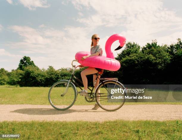 young woman on bicycle with flamingo ring - offbeat imagens e fotografias de stock