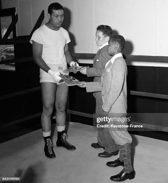 Après son entraînement, le boxeur américain noir Joe Louis reçoit deux jeunes admirateurs auxquels il remet des livres dédicacés qu'ils ont intitulés...