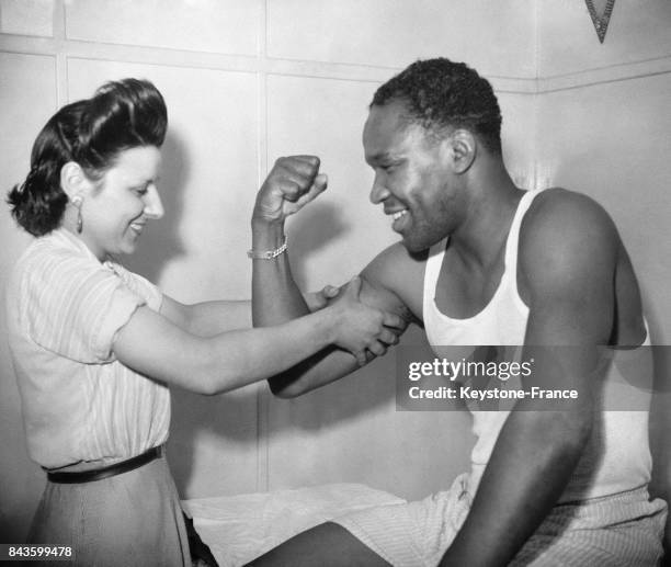 La secrétaire du masseur Straboni admire les muscles de Holman Williams, boxeur, avant que celui-ci n'affronte Marcel Cerdan sur le ring, en 1946 à...