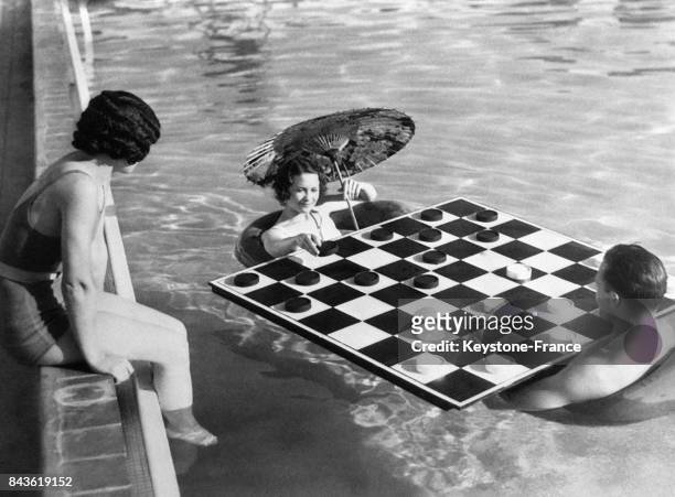Deux joueurs sur des bouées jouent aux dames dans une piscine sous l'oeil attentif d'une spectatrice assise sur le rebord le 10 janvier 1933 en...