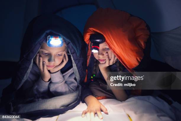 bambini che leggono un libro in campeggio di notte - torcia elettrica foto e immagini stock