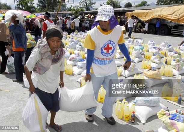 Local Red Cross volunteer helps an evacuee carry sack of rice during a food distribution by the International Committee of the Red Cross on January...
