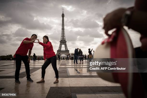 Couple forms a heart with their hands as they pose in front of the Effeil Tower on the Place du Trocadero in Paris on September 7, 2017. / AFP PHOTO...