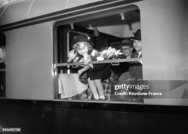 Petite fille avec un bouquet de fleurs saluant à la fenêtre d'un wagon, à Paris, France, avril 1936.