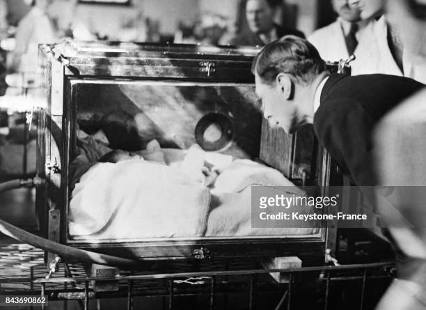 Le Duc d'York, futur George VI, examinant un nourrisson dans une couveuse à l'occasion d'une visite au 'Queen's hospital', un hôpital pour enfants, à...