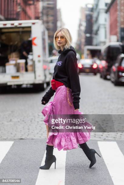 Lisa Hahnbueck wearing a black hoody with the print lovers, red Gucci velvet belt bag, pink ruffled skirt with slit, black ankle boots, vogue eyewear...