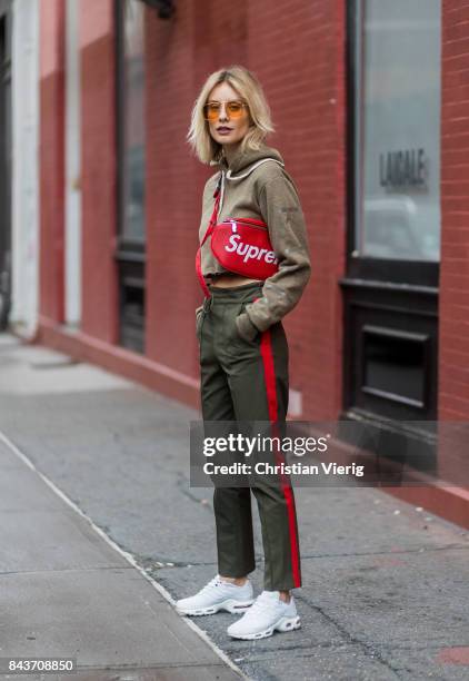 Lisa Hahnbueck wearing red Supreme x Louis Vuitton bag, khaki hoody, sweater pants with stripes, sneakers, vogue eyewear x Gigi Hadid sunglasses on...