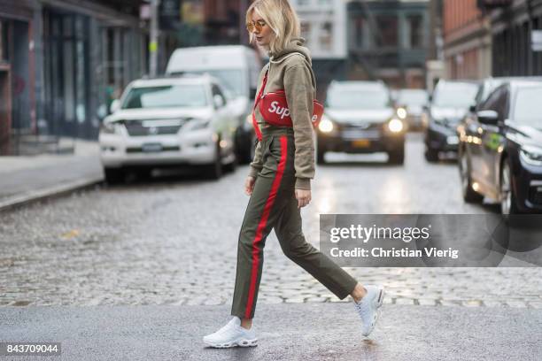 Lisa Hahnbueck wearing red Supreme x Louis Vuitton bag, khaki hoody, sweater pants with stripes, sneakers, vogue eyewear x Gigi Hadid sunglasses on...