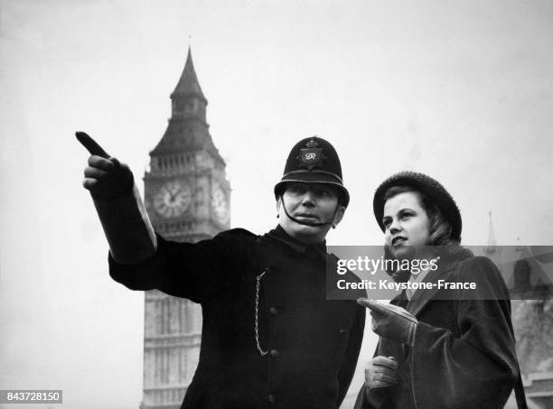 Un police montre du doigt la destination à prendre à une jeune femme, à Londres, Royaume-Uni le 27 mars 1949.