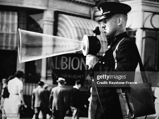 Un agent de la circulation tenant dans la main un mégaphone indique aux piétons quand ils peuvent traverser, à Londres, Royaume-Uni en août 1938.