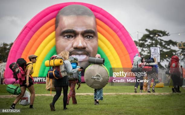 People pass a giant inflatable face of Kanye West as they arrive on the first day of the Bestival festival being held at the Lulworth Estate on...