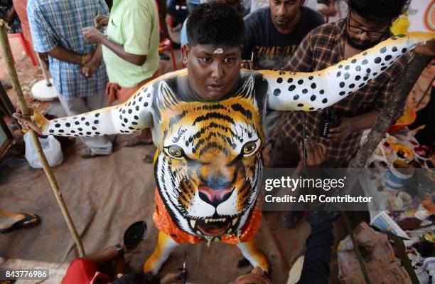 An Indian boy stands still while his body is painted ahead of the 'Pulikali', or Tiger dance, in Thrissur on September 7, 2017. The folk-art event is...