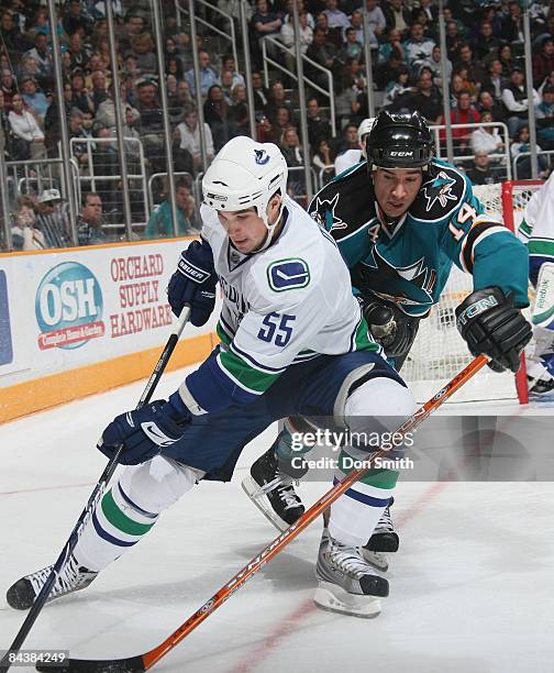 Shane O'Brien of the Vancouver Canucks tries to control the puck by the boards while Jonathan Cheechoo of the San Jose Sharks tries to reach over and...