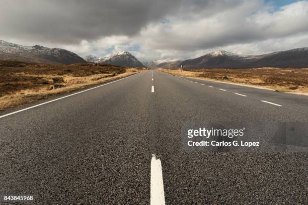 empty road leading to snowy mountains in the glen coe valley - diminishing perspective stock pictures, royalty-free photos & images