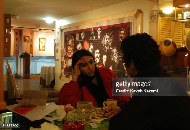 Dating couple sit in a cafe in central Tehran drinking coffee, 17th March 2004. Behind them is a large noticeboard covered with pictures of famous...