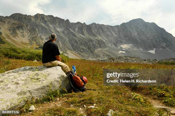 Hiker George Nick sits on a rock waiting for his climbing partner to return near Capitol Lake with the massive Capitol Peak in front of him on...