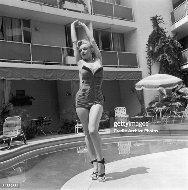 American actress Marilyn Monroe stands next to a swimming pool in a strapless swimsuit and high heels, circa 1951.