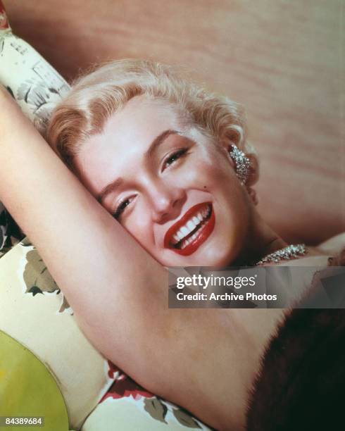 American actress Marilyn Monroe lies smiling on a couch, circa 1955.