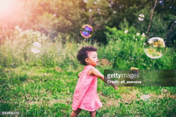 meisje van de afro-amerikaanse baby spelen met zeepbellen in het park - baby sommer stockfoto's en -beelden