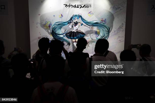 Attendees take photographs of a figure of Hatsune Miku, a virtual pop star and the voice behind Crypton Future Media Inc.'s vocal synthesizer...