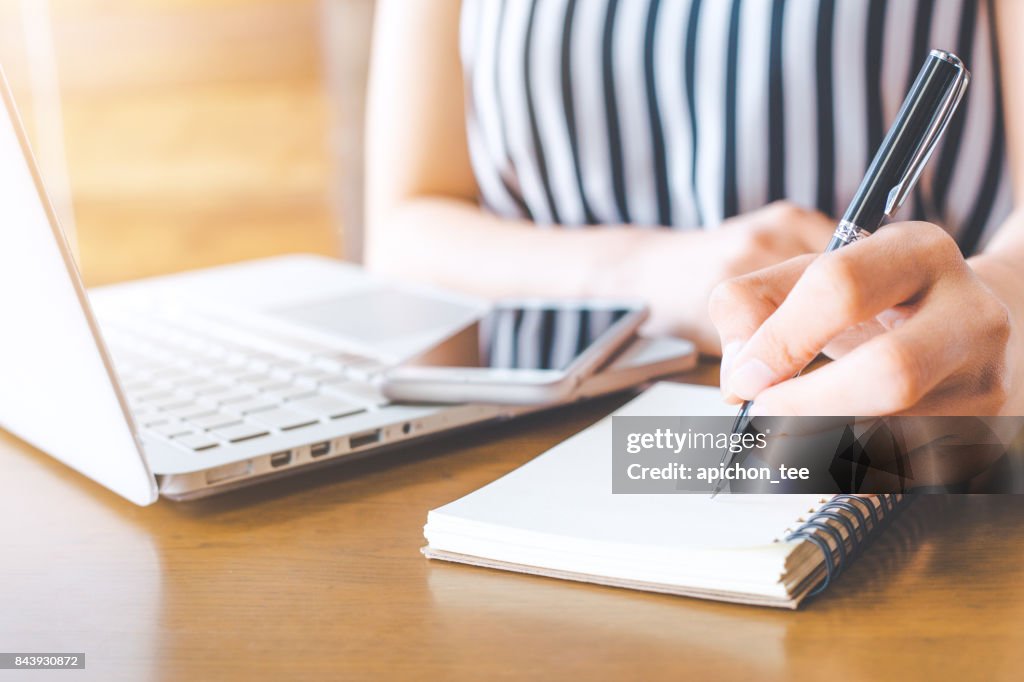 Unternehmen Frau Hand Arbeit am Computer und schreiben auf ein Noteped mit einem Stift im Büro.