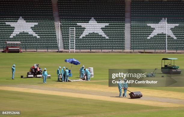 This picture taken on September 7, 2017 shows ground staff preparing the cricket pitch of the Gaddafi Stadium in Lahore. Groundsmen are rolling down...