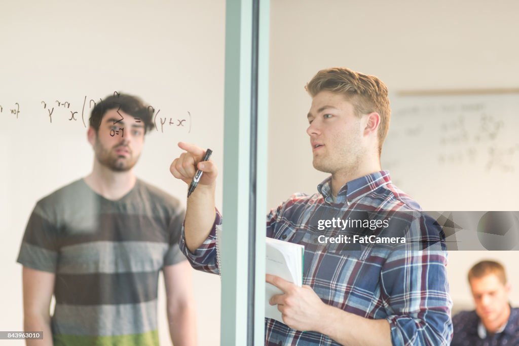 Students work on math problem together in conference room. They are writing the equation on the whiteboard