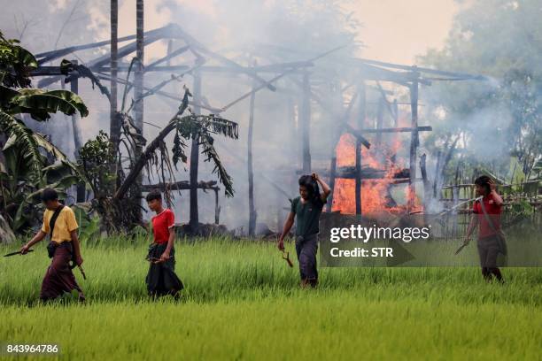 In this photograph taken on September 7 unidentified men carry knives and slingshots as they walk past a burning house in Gawdu Tharya village near...