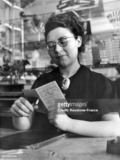 Une buraliste poinçonne la carte de rationnement d'un fumeur avant de lui remettre du tabac, à Riom en France, en 1942.