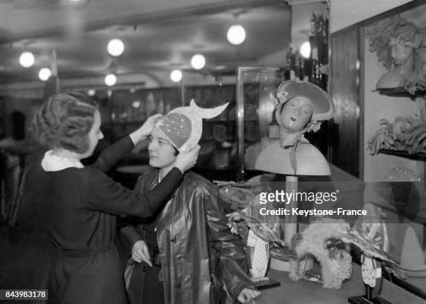 Une catherinette essaie un chapeau chez un couturier en prévision de la fête de Sainte-Catherine le 22 novembre 1932 à Paris, France.