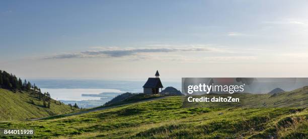 panoramic view of steinling alm chapel below kampenwand mountain with lake chiemsee in the distance, chiemgau, upper bavaria, germany - chiemsee photos et images de collection