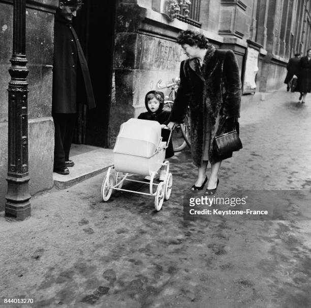 Femme et son enfant poussant un landau devant le regard attendri d'un policier, à Paris, France en 1956.