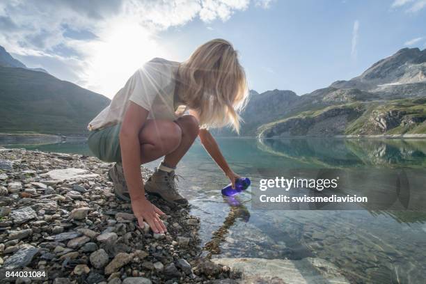 hiking blond girl filling bottle from mountain lake - purity stock pictures, royalty-free photos & images