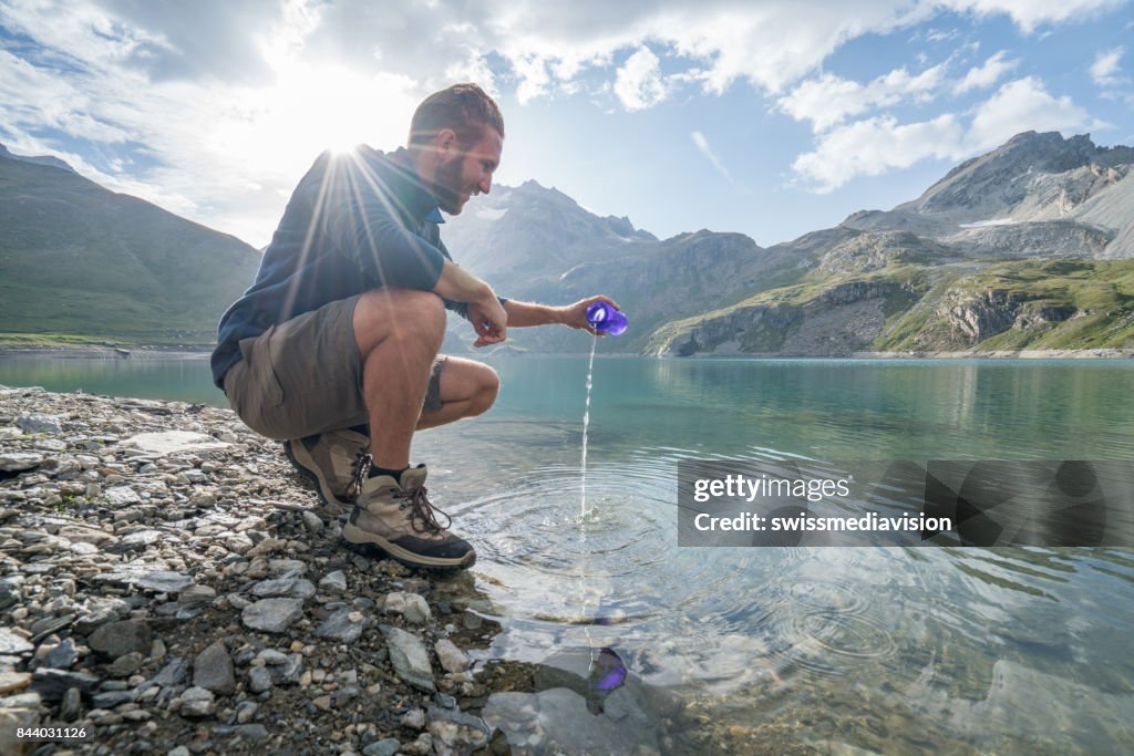 Hiking male filling bottle from mountain lake