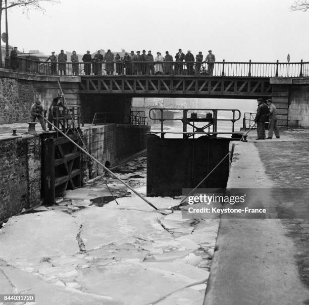 Les éclusiers du Canal Saint-Martin, munis de perches, aident à l'écoulement des glaçons déjà disloqués par le dégel, à Paris, France le 28 février...