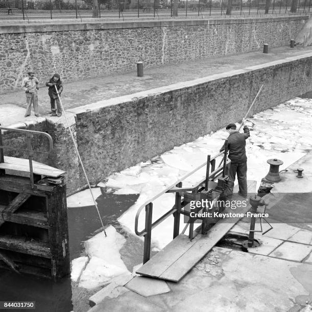 Les éclusiers du Canal Saint-Martin, munis de perches, aident à l'écoulement des glaçons déjà disloqués par le dégel, à Paris, France le 28 février...