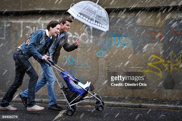 couple pusing a pram in the rain - mother protecting from rain stock-fotos und bilder
