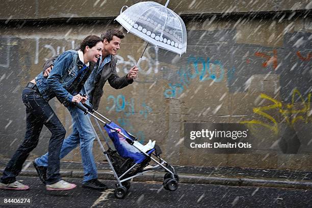 couple pusing a pram in the rain - mother protecting from rain stock pictures, royalty-free photos & images