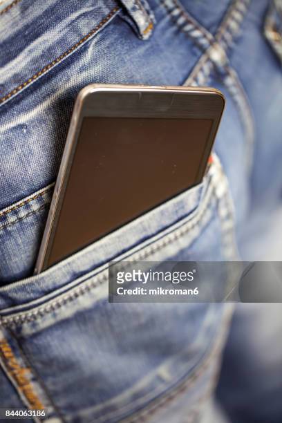 man putting mobile phone into back pocket blue jeans - phone in back pocket stock pictures, royalty-free photos & images