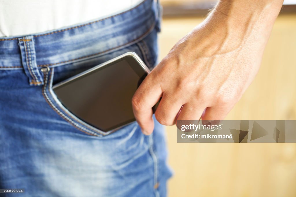 Man Putting Mobile phone Into Back Pocket blue jeans